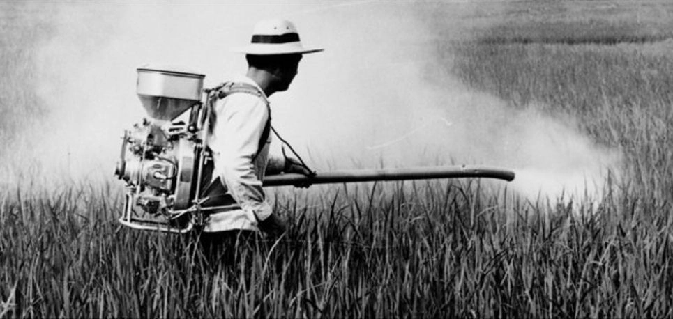 an old photo of a farmer using leaf blower to spray pesticides on the farm