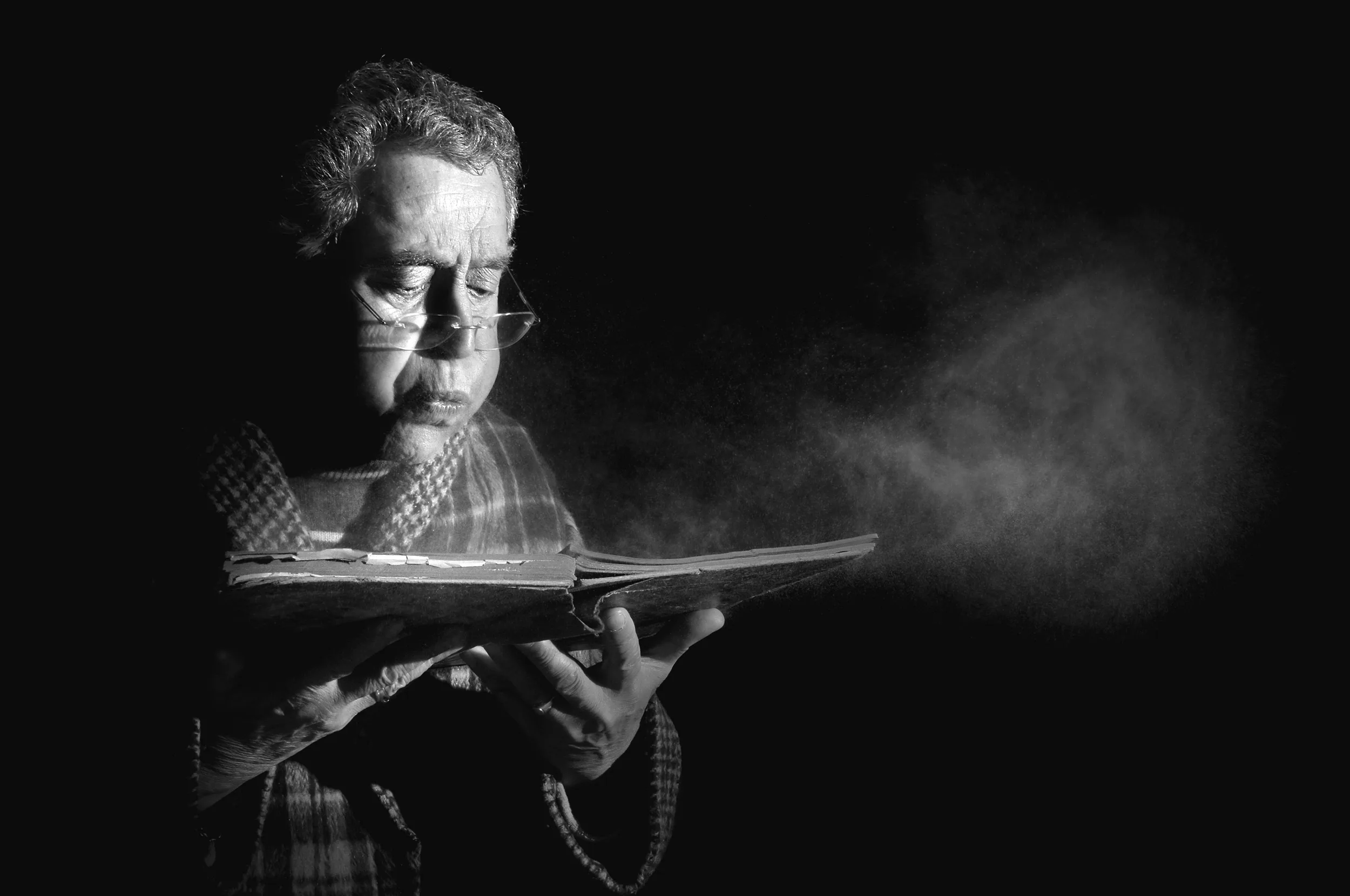 An old photo of a man blowing dust off a book