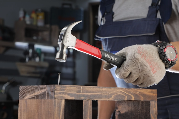 A claw hammer is being used to drive a nail into wood