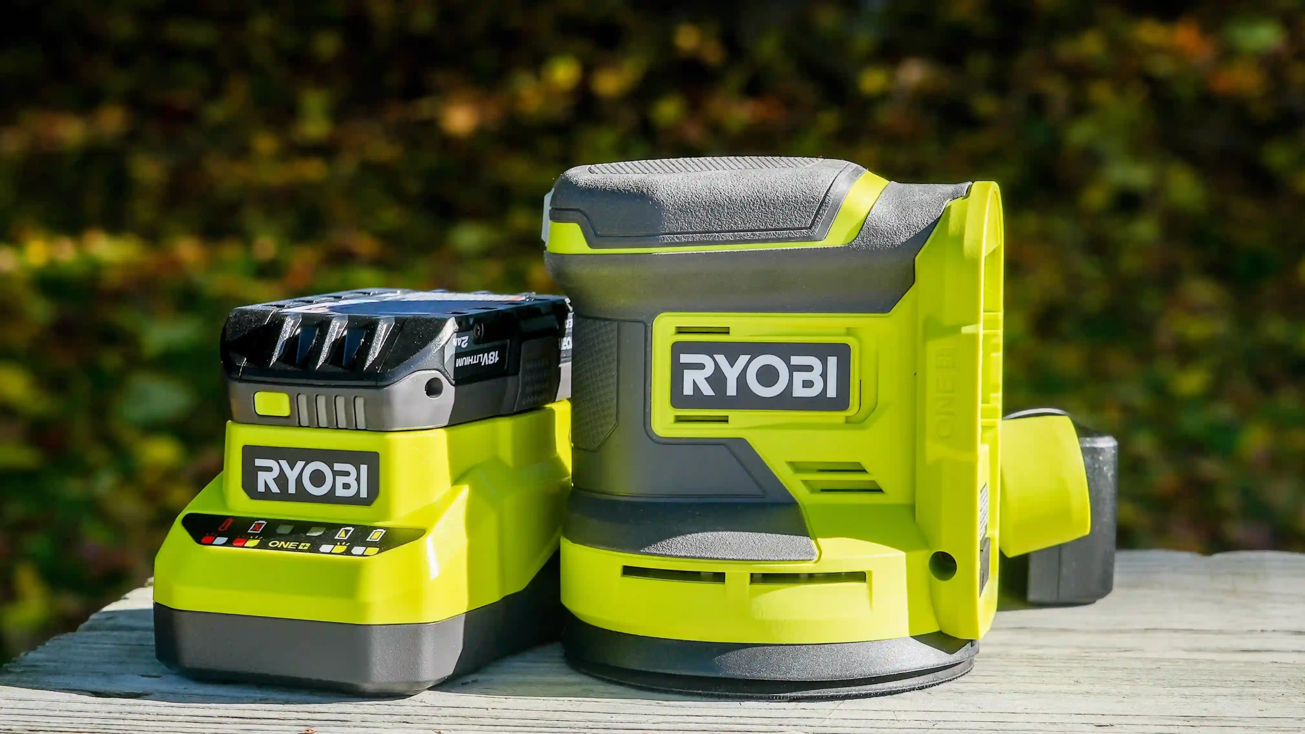 a Ryobi cordless sander and its accompanying battery, set on an outdoor surface.