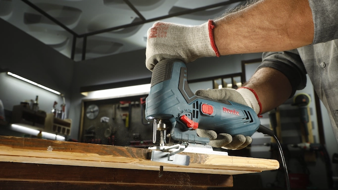 a person using a Ronix jigsaw to cut wood in a workshop while wearing protective gloves