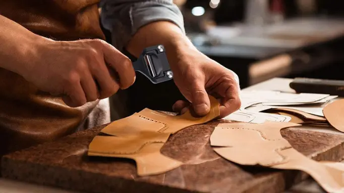 A man using a leather skiver on a piece of leather with patterns on it