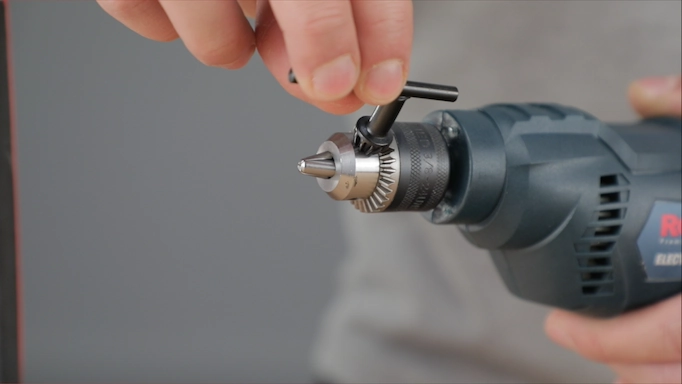 A chuck key being used on a drill chuck to insert a drill bit