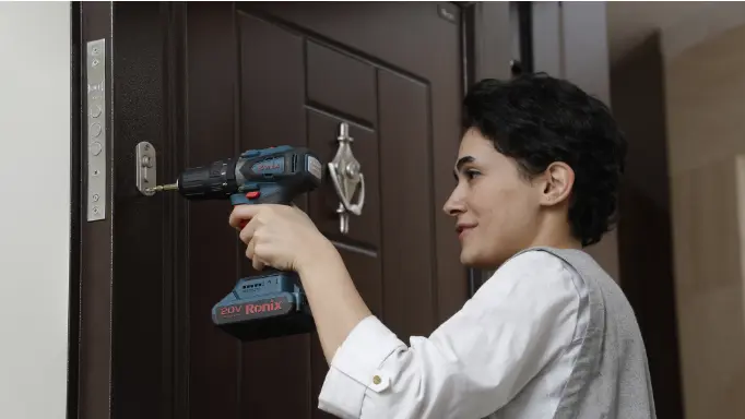 A woman tightening the door lock using a Ronix cordless screwdriver
