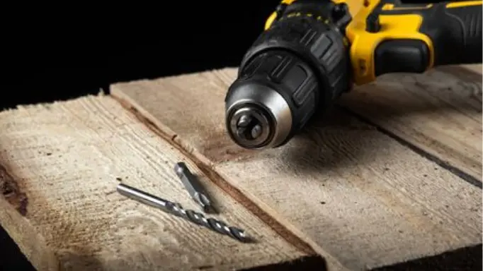 A cordless screwdriver with a screwdriver and a drilling bit in front of it