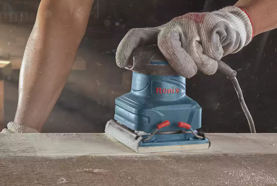 A carpenter using sander on a wood piece with safety gloves