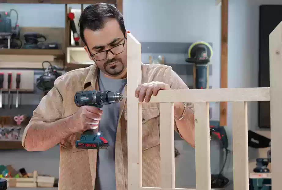 A man using an impact driver to assemble a wooden bed