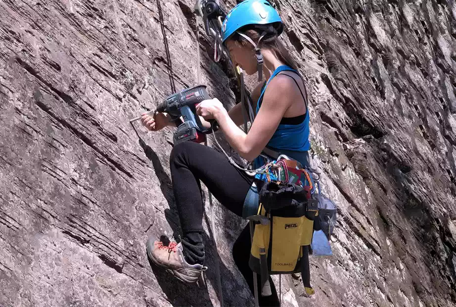 A woman using a rotary hammer while rock climbing
