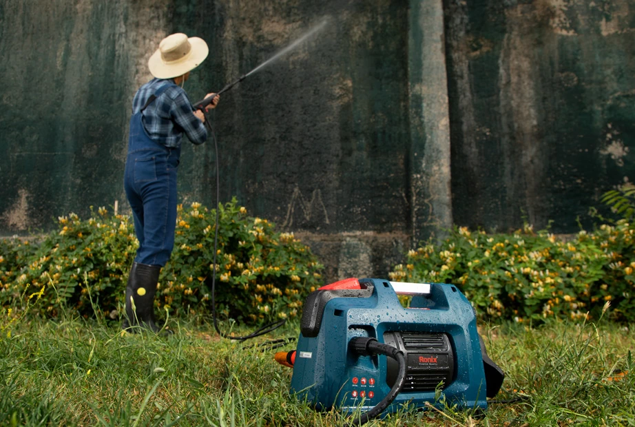  A man using a high-pressure washer to wash the dirt off a wall outdoors