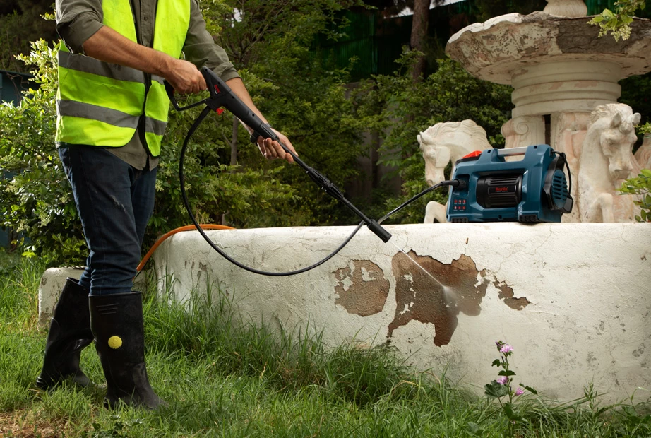 A man using a high-pressure washer to remove the peeling paint