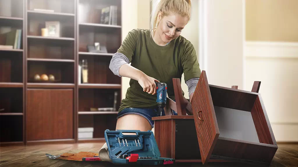 A woman using a mini electric screwdriver to assemble a chest of drawers