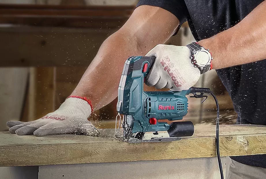 A man using a jigsaw wearing protective gloves