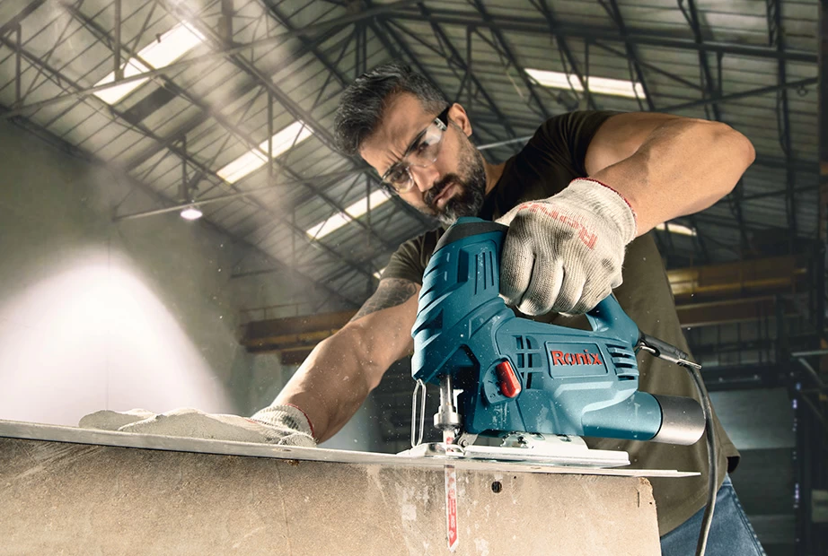 A man cutting through wood with a Ronix 4150 electric jigsaw in an industrial shed