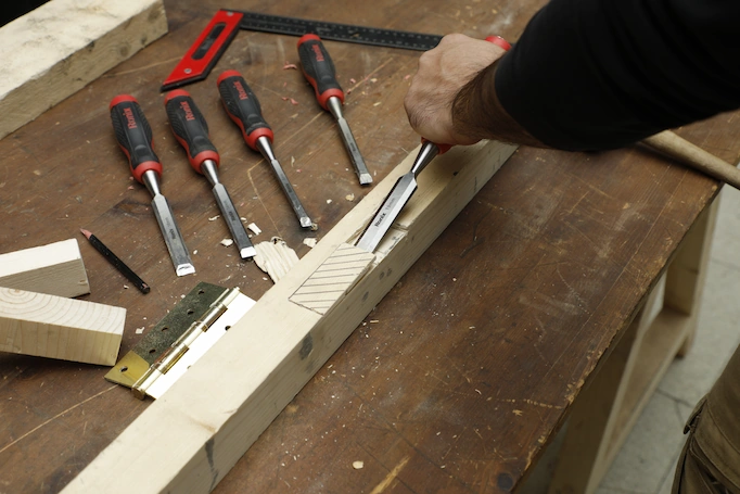 A collection of chisels resting on the table and a chisel being used