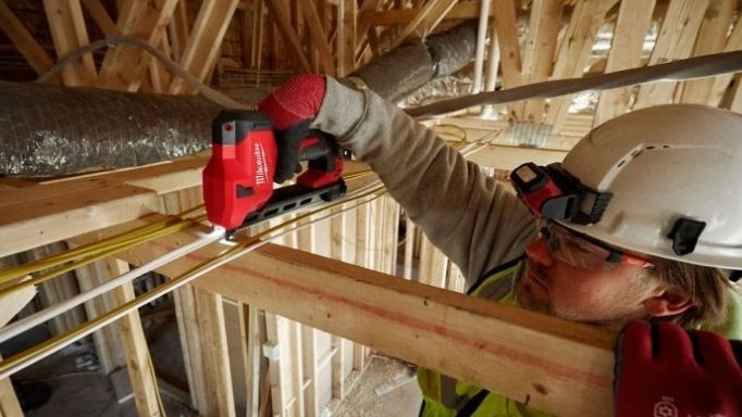 A man using a Makita staple gun on cables in the ceiling