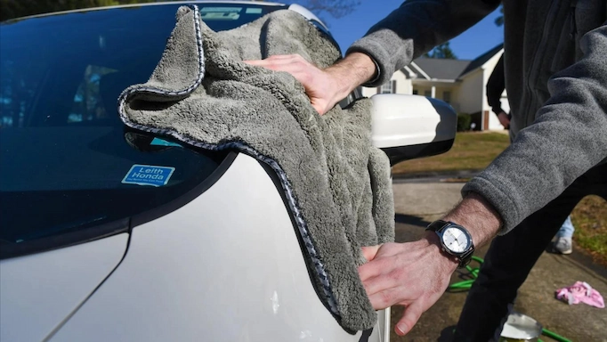 A microfiber towel is used to dry a car after washing