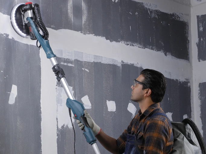 A man sanding a wall with a drywall sander