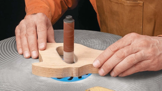a man using a spindle sander to shape a piece of wood