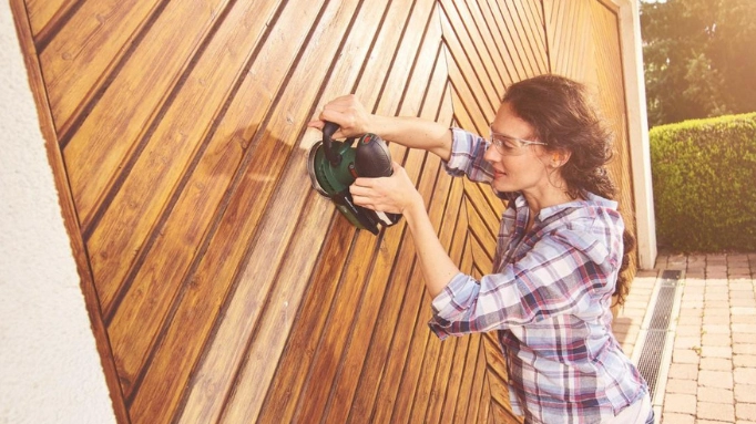 a woman using a sander for sanding a wooden wall