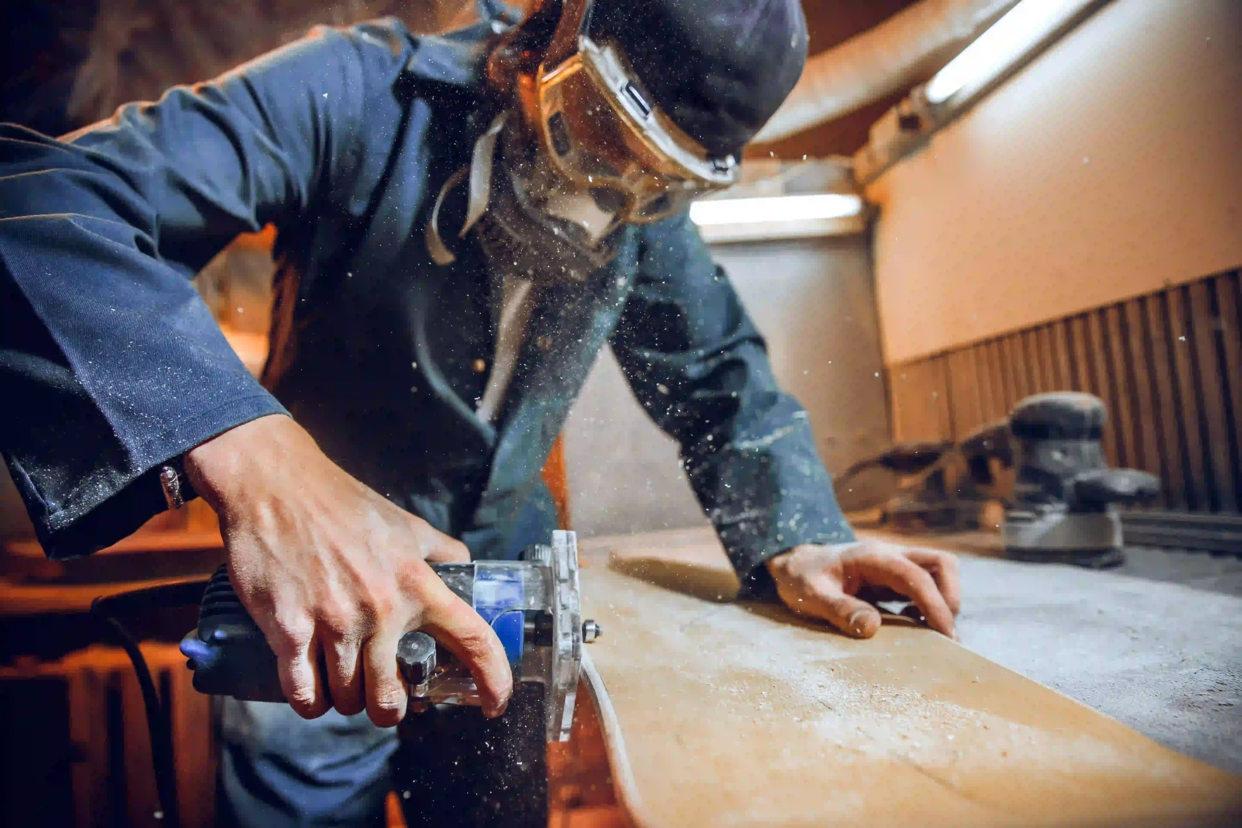 A close-up of a carpenter in safety gear, operating a circular saw to cut wooden boards, with sawdust flying in a workshop