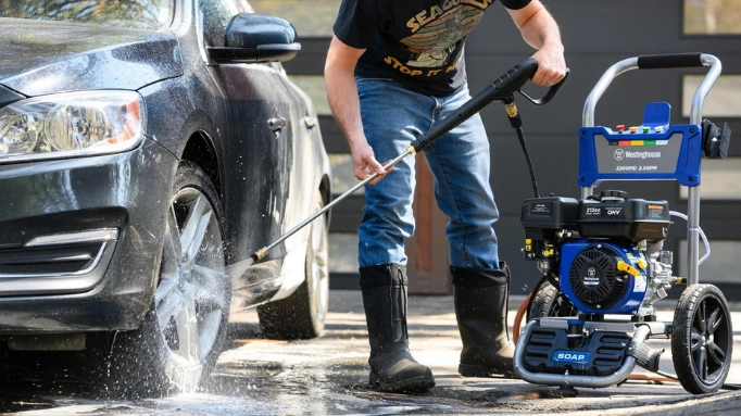 A man using a pressure washer for washing a car