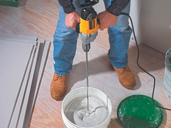 A man blending plaster with a paddle mixer