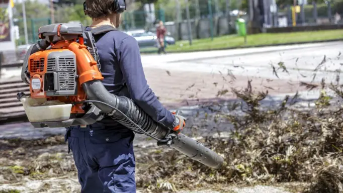 A man using a gas backpack leaf blower to cleanup the fallen leaves on the street