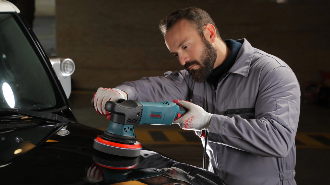 A car detailer is operating the Ronix 6122 dual-action orbital polisher on a car