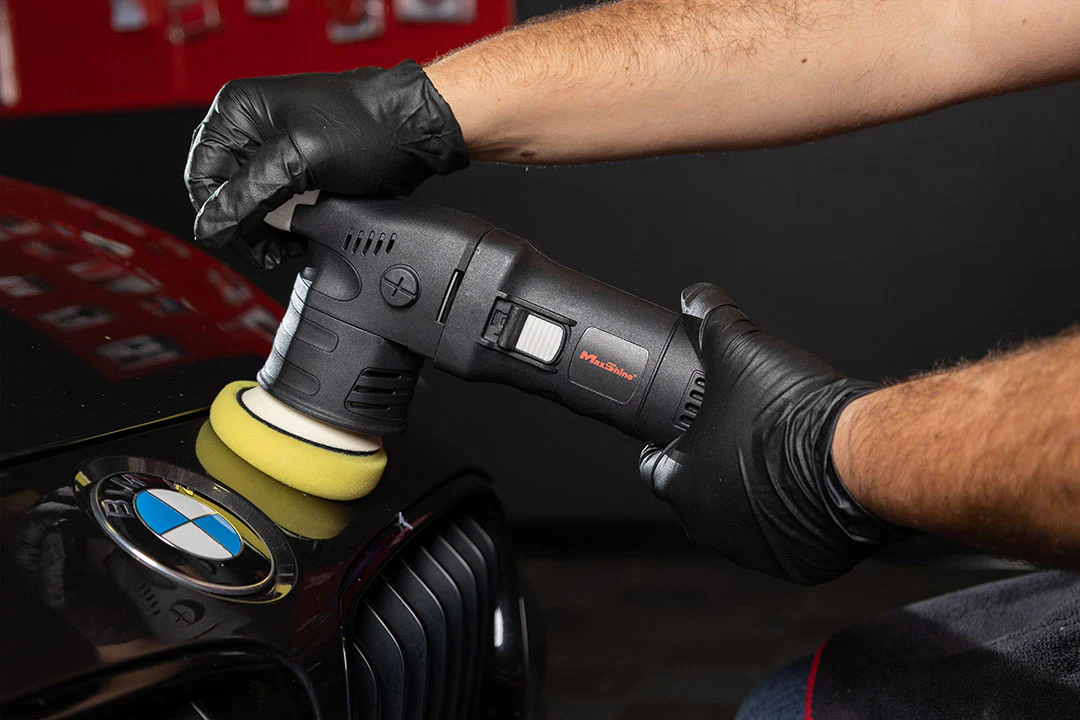 hands of an operator using an orbital polisher to detail a BMW