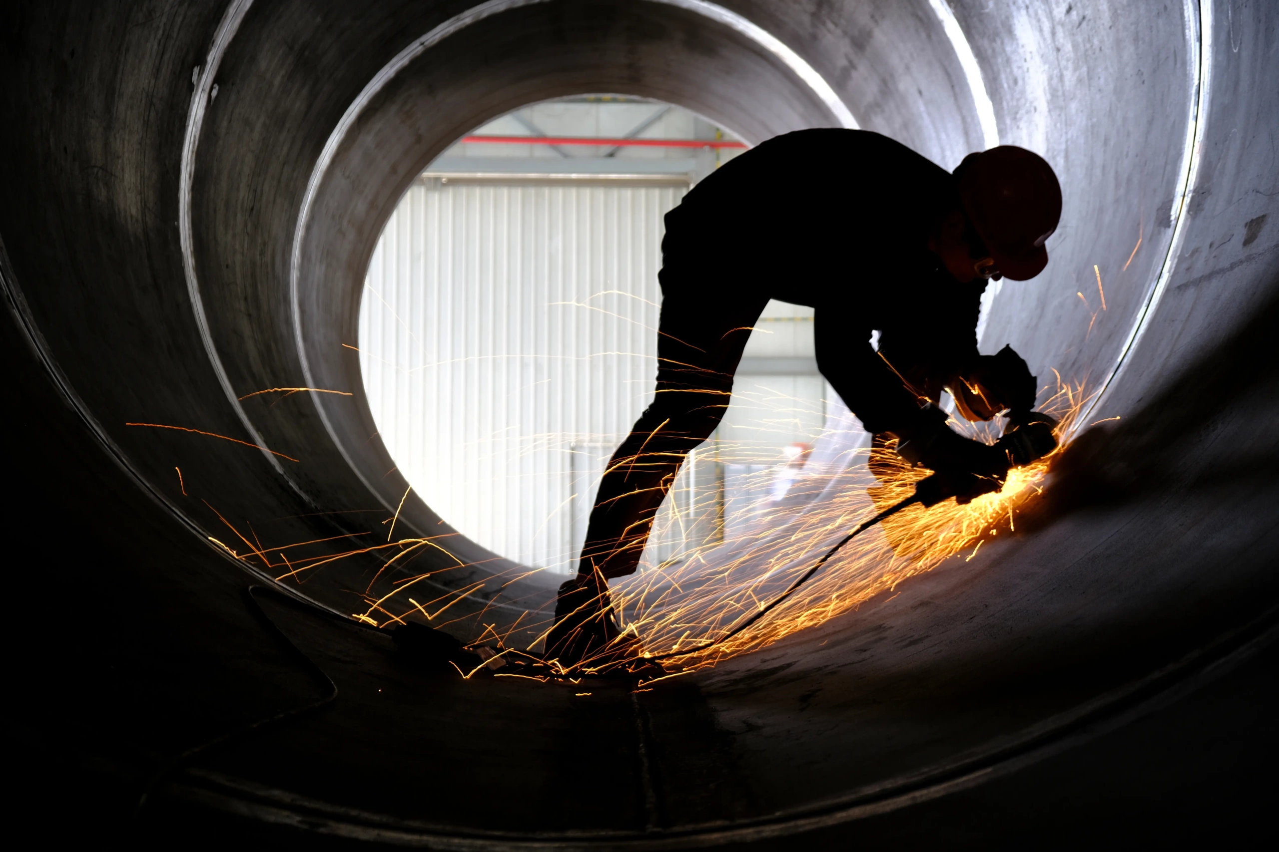 A worker using and angle grinder in a huge pipe