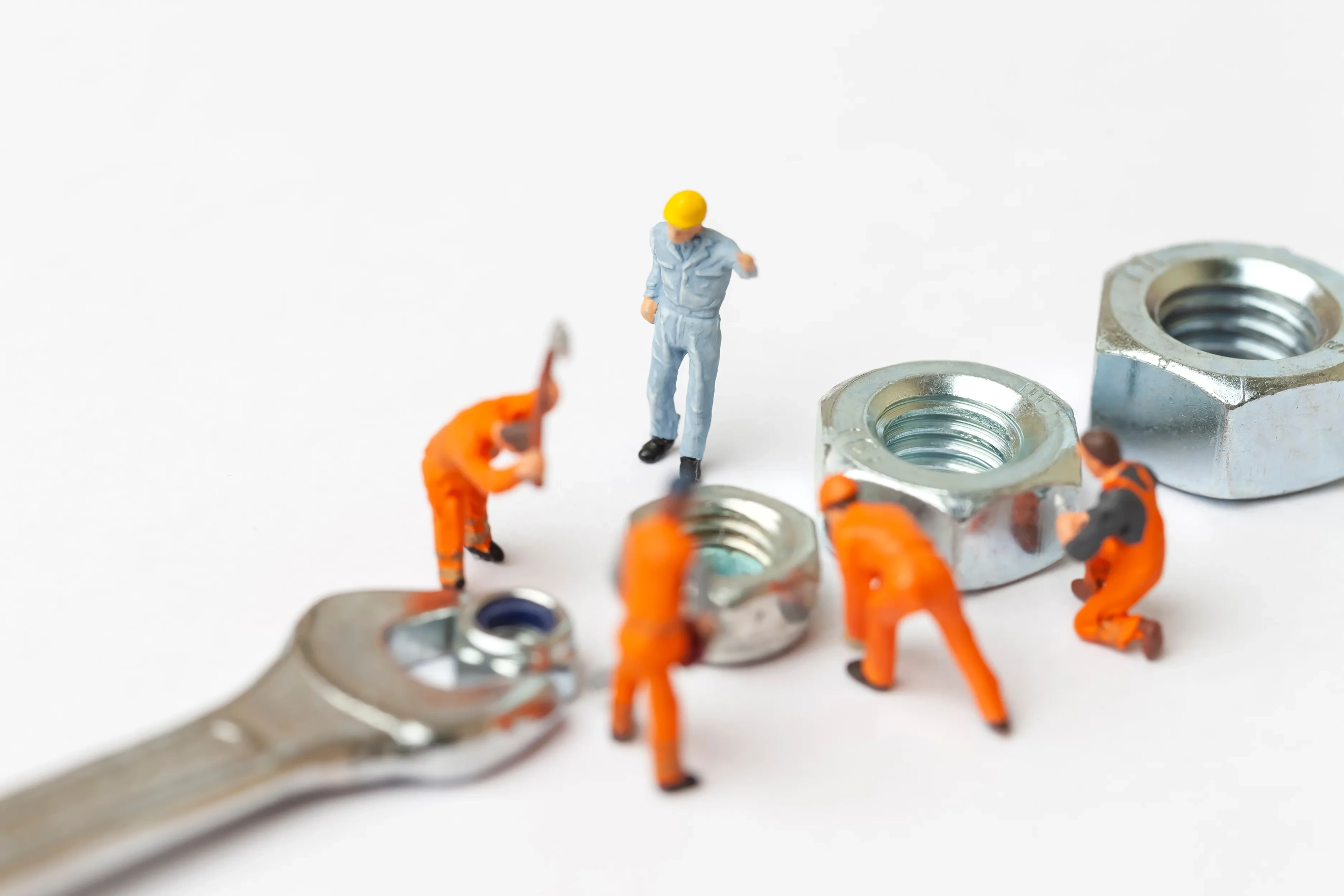 Little miniature workers and an engineer working on a wrench and some nuts