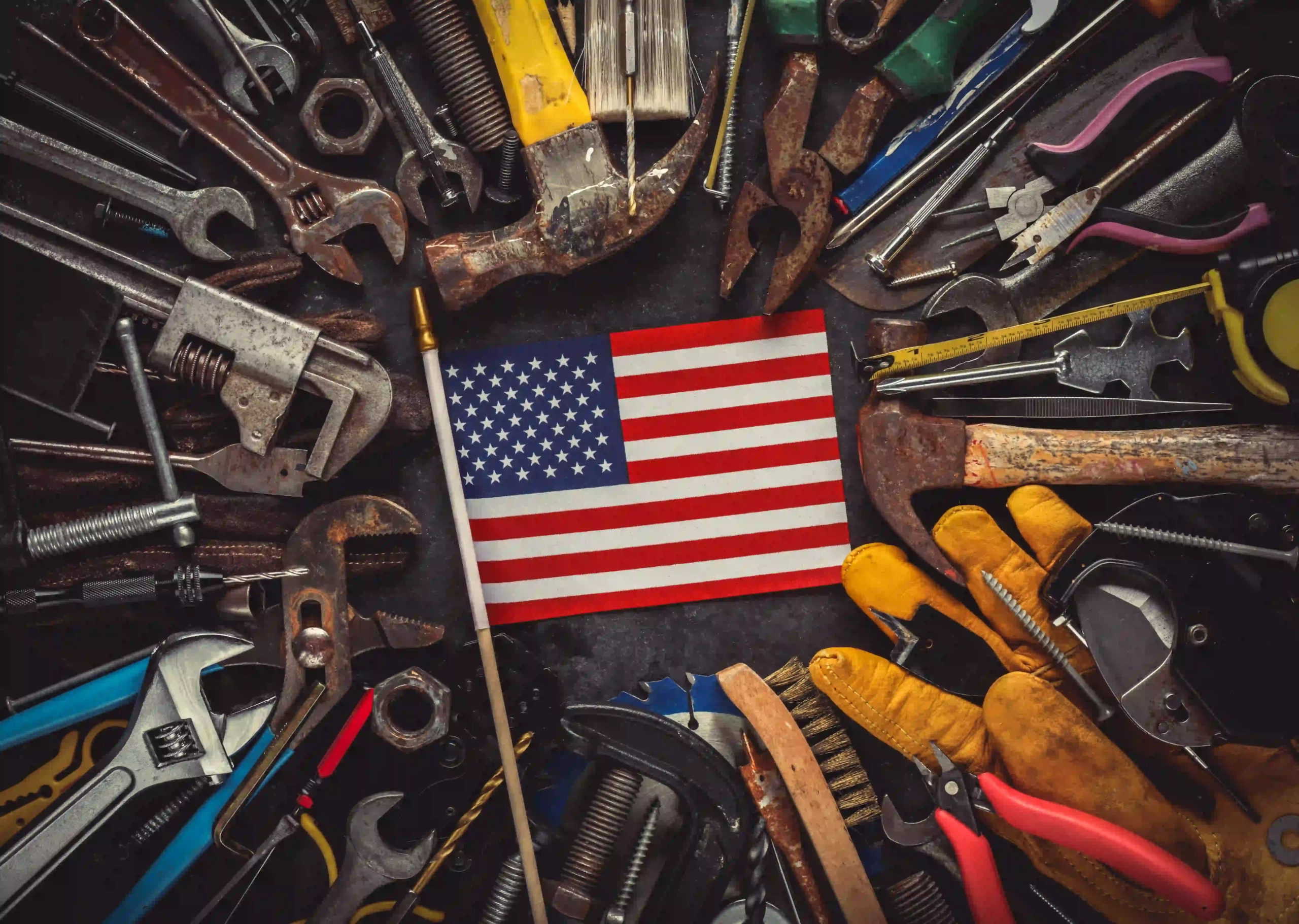 Hand tools like wrenches, hammers, pliers surrounding an American flag.