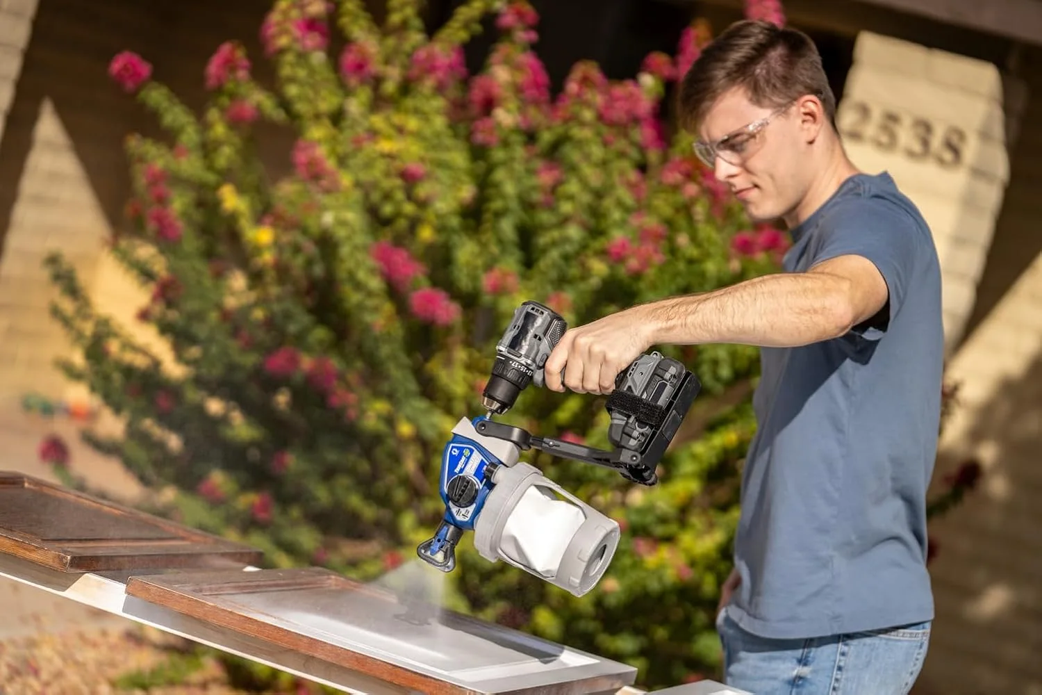 Man using a cordless paint sprayer to paint a surface outdoors.