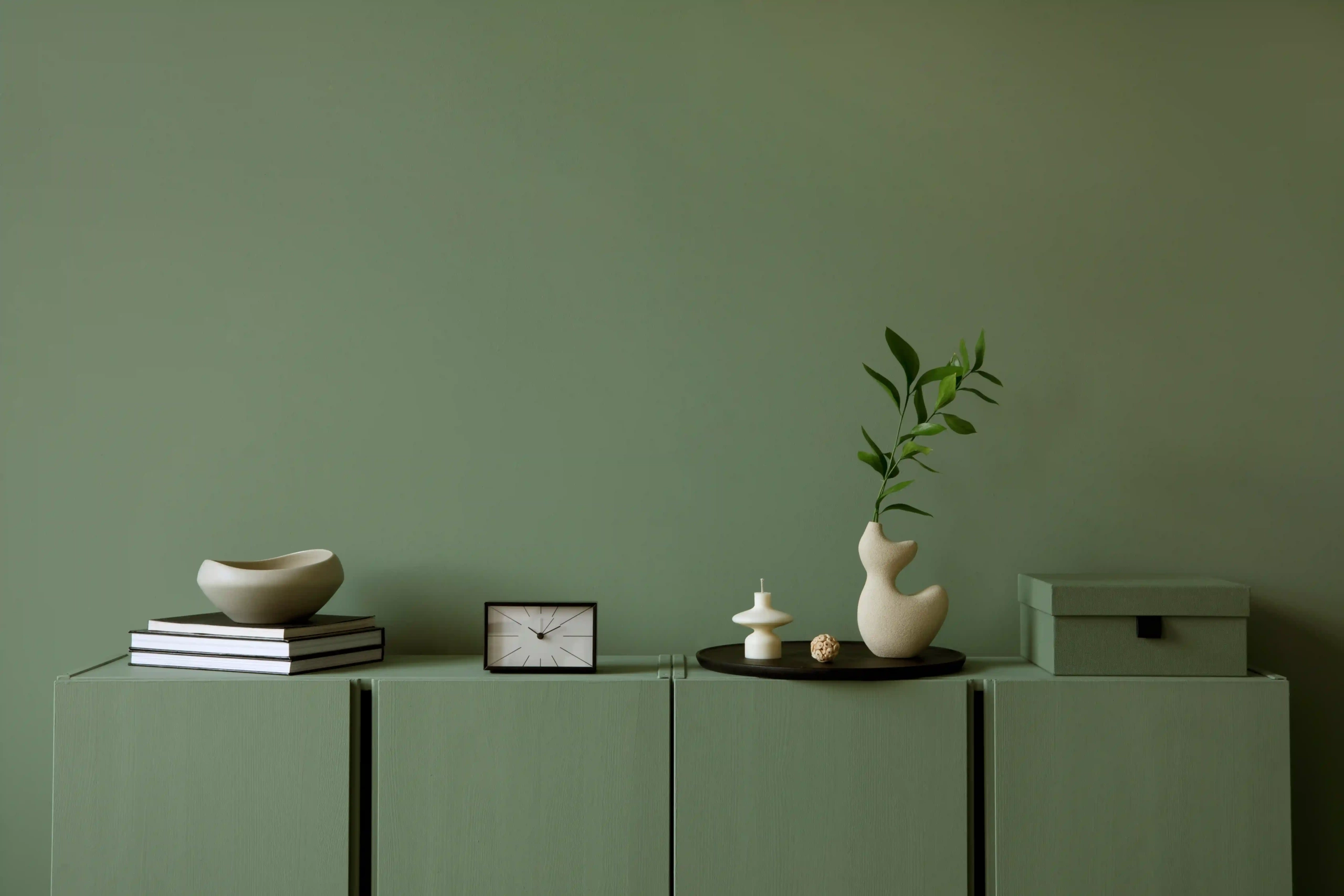 Minimalistic interior with a green-painted wall and decor on a matching green cabinet.