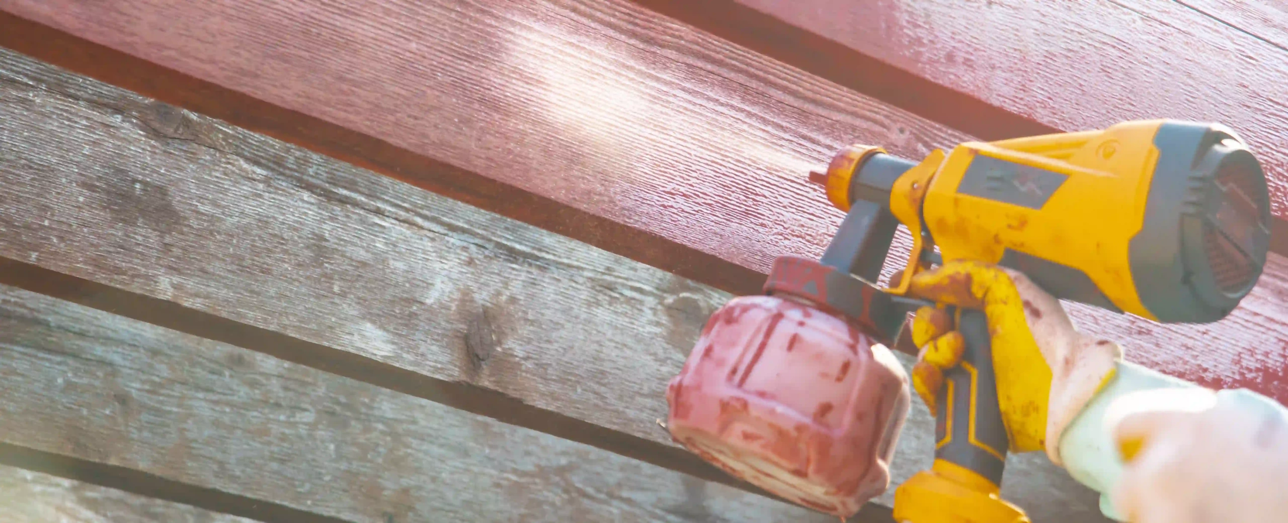 Close-up of a cordless paint sprayer painting a wooden surface red.