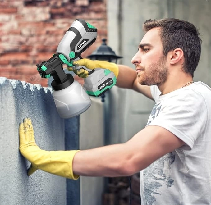 Man using a cordless paint sprayer to paint a concrete surface outdoors.