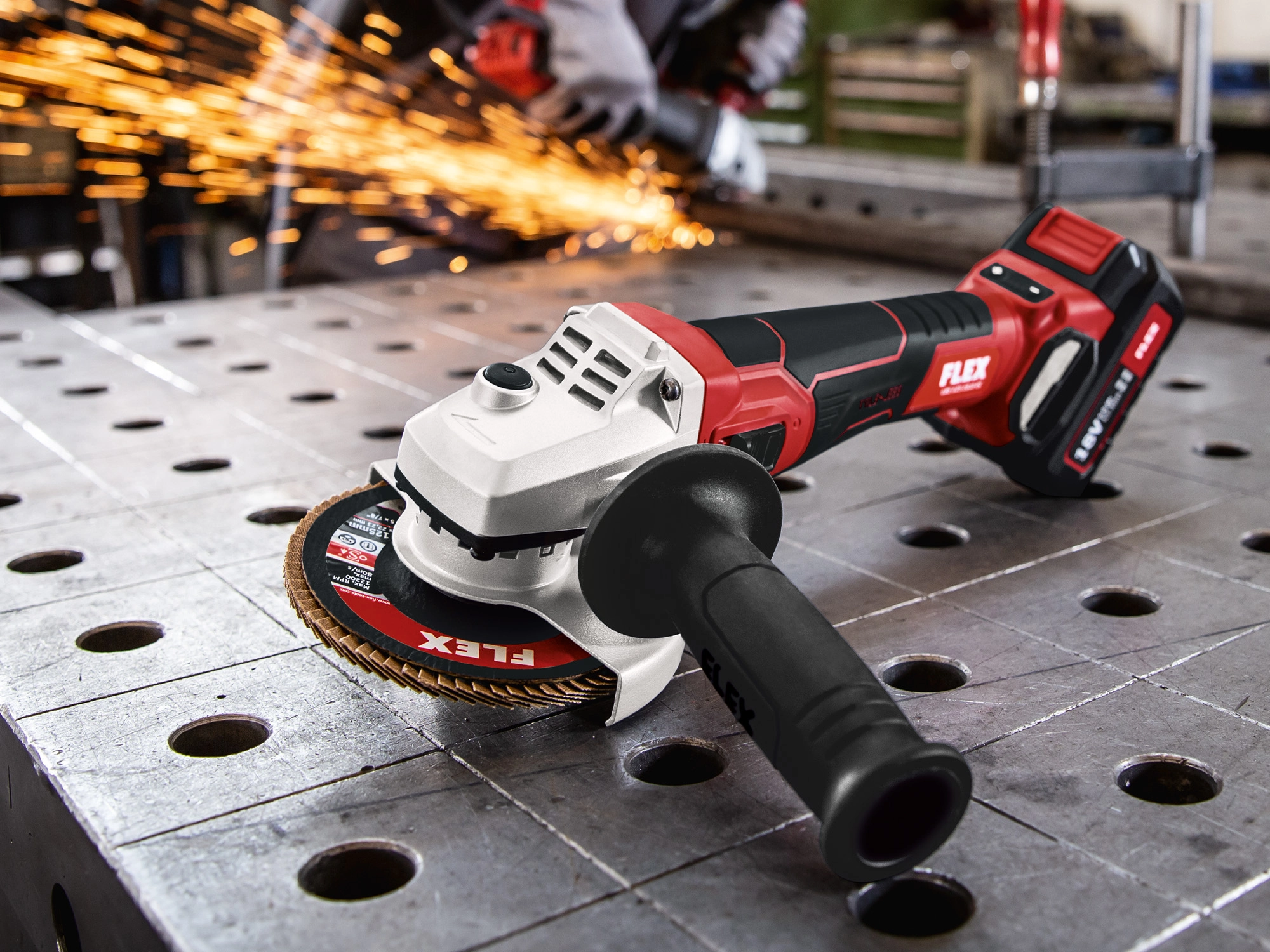 Flex cordless angle grinder on metal in the foreground with sparks in the background.