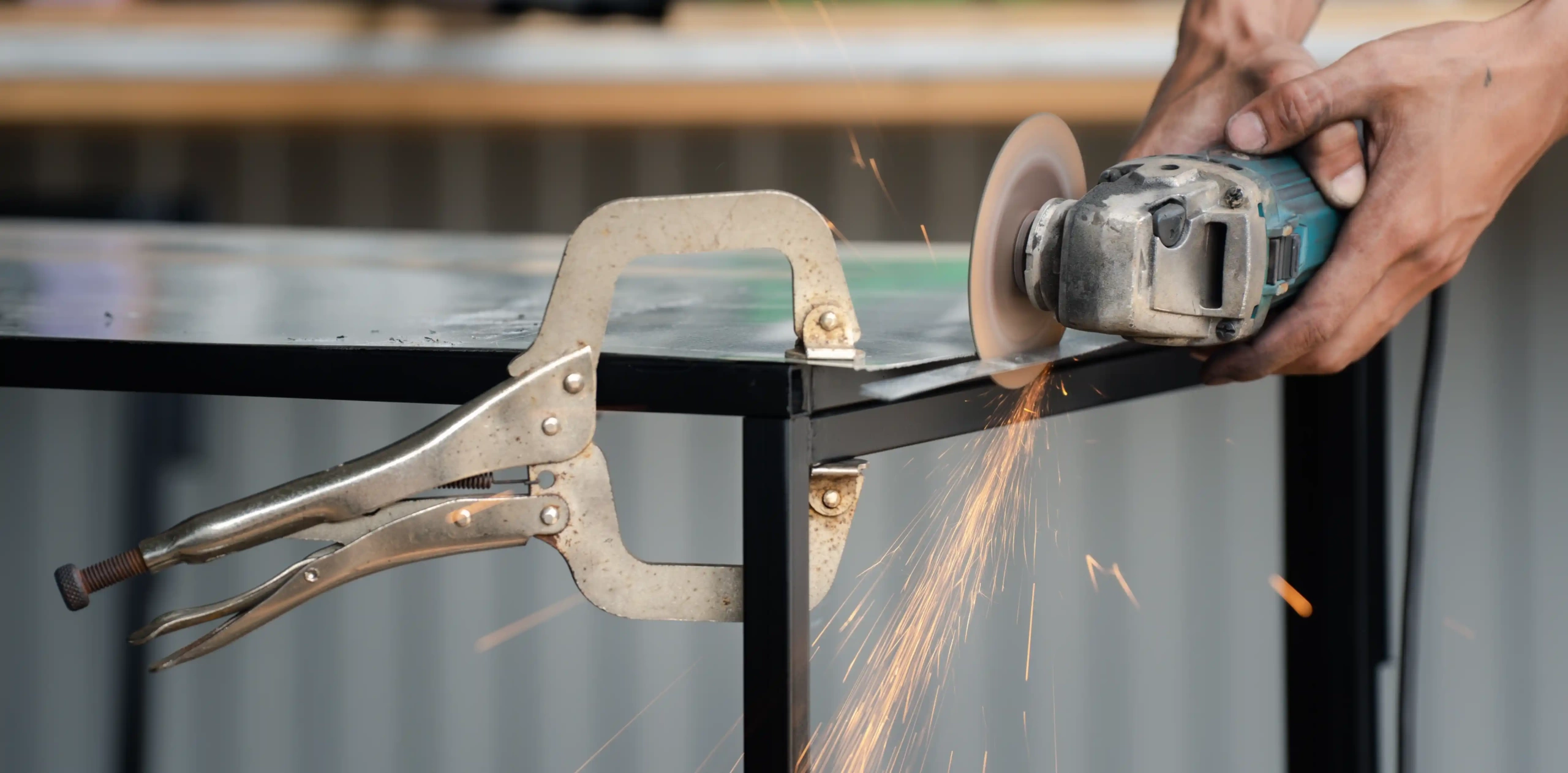 Locking pliers securing a metal sheet while a grinder produces sparks