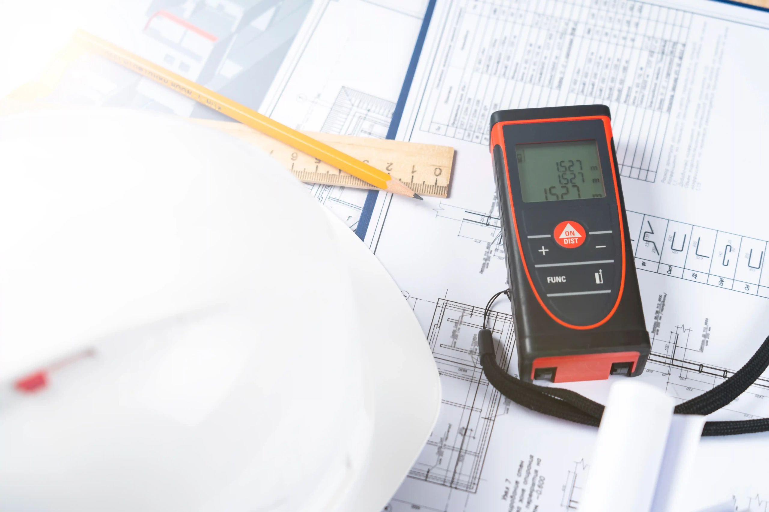 A laser tape measure next to a ruler, pen and a helmet