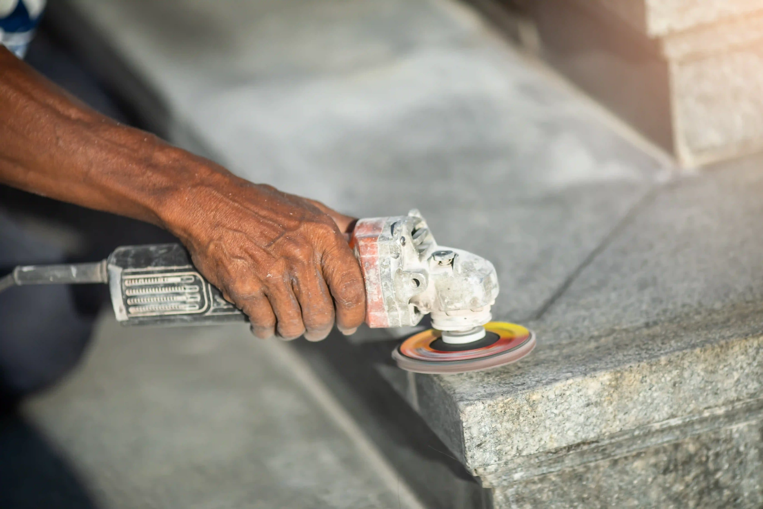 Worker using an angle grinder to smooth a granite edge.