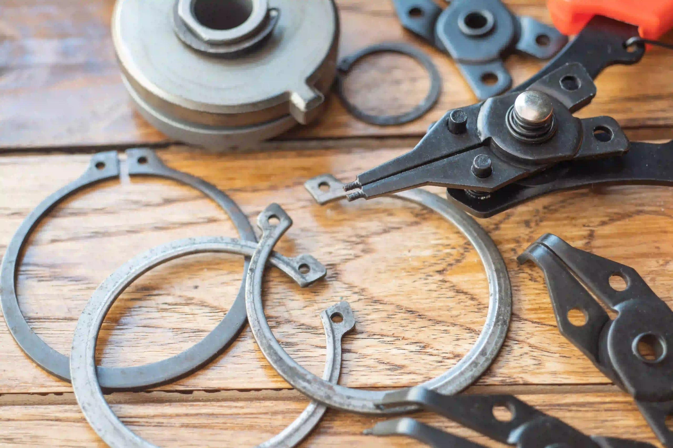 snap ring pliers gripping a circlip, with various snap rings on a wooden surface.