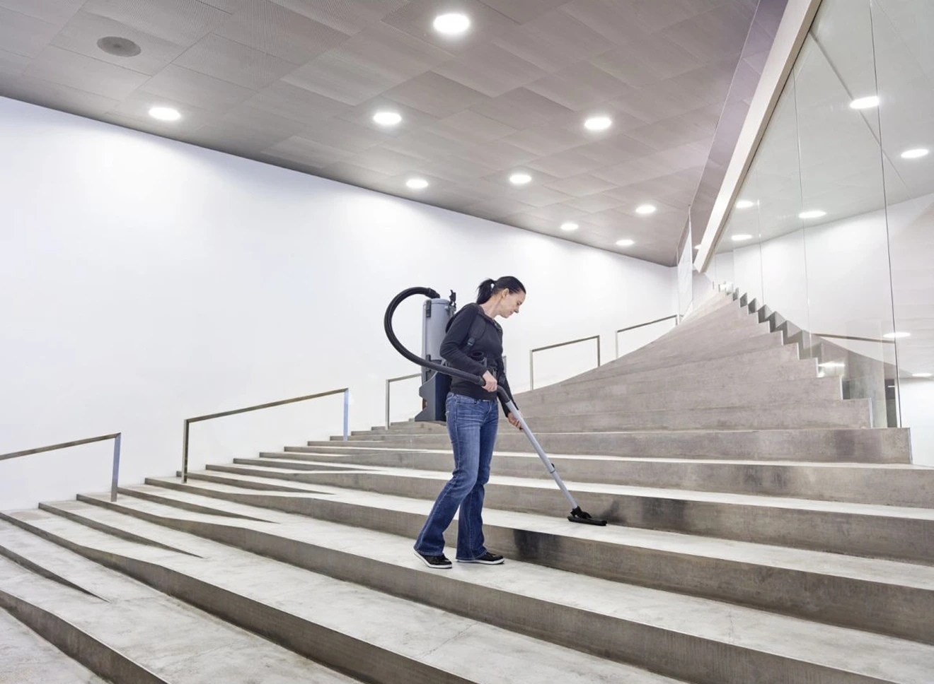 A woman is vacuum cleaning the stairs in a large commercial area