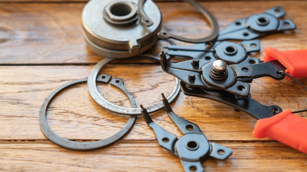 snap ring pliers gripping a circlip, with various snap rings on a wooden surface.