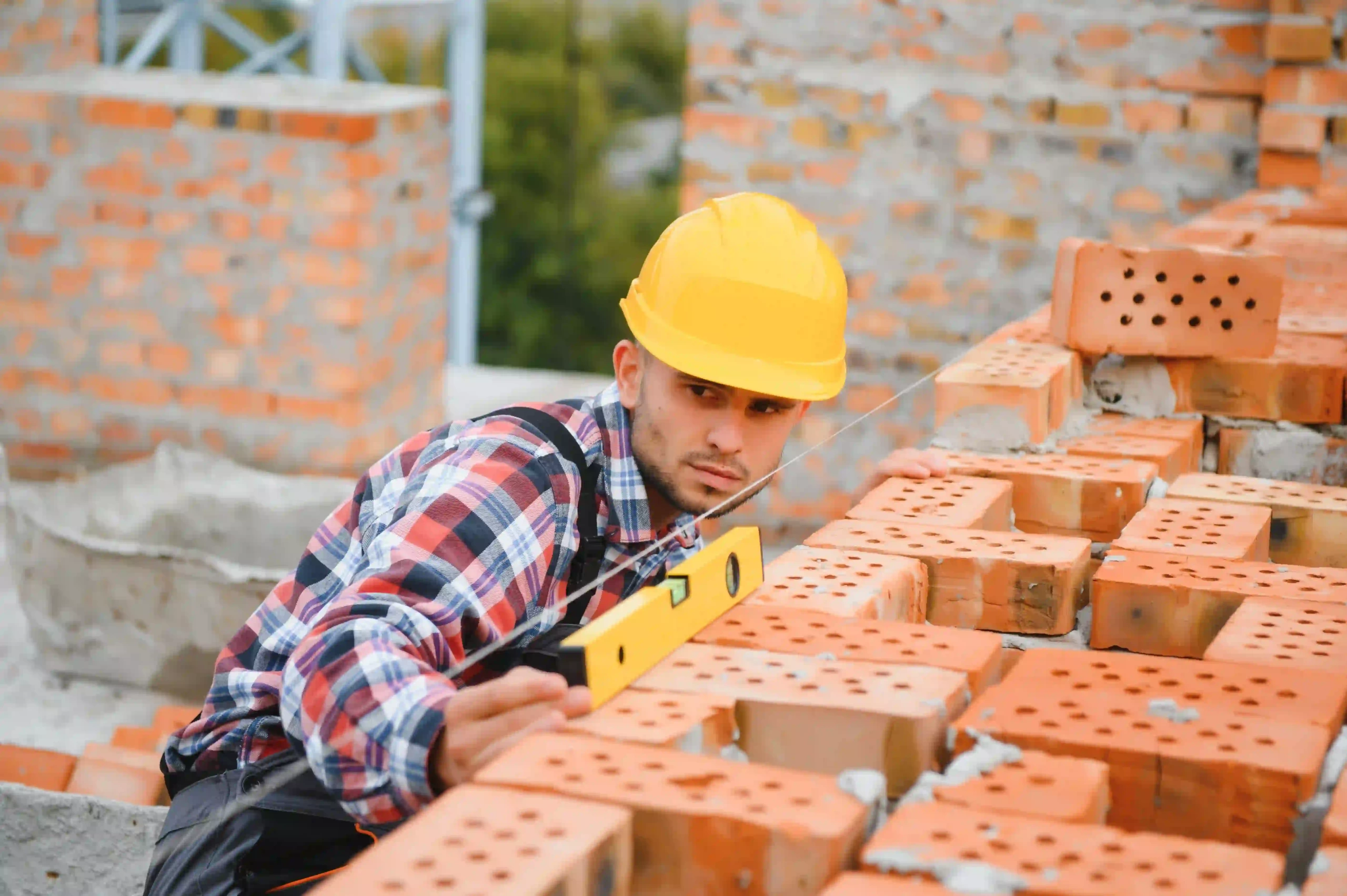 Bricklayer using a spirit level to align bricks at a construction site.