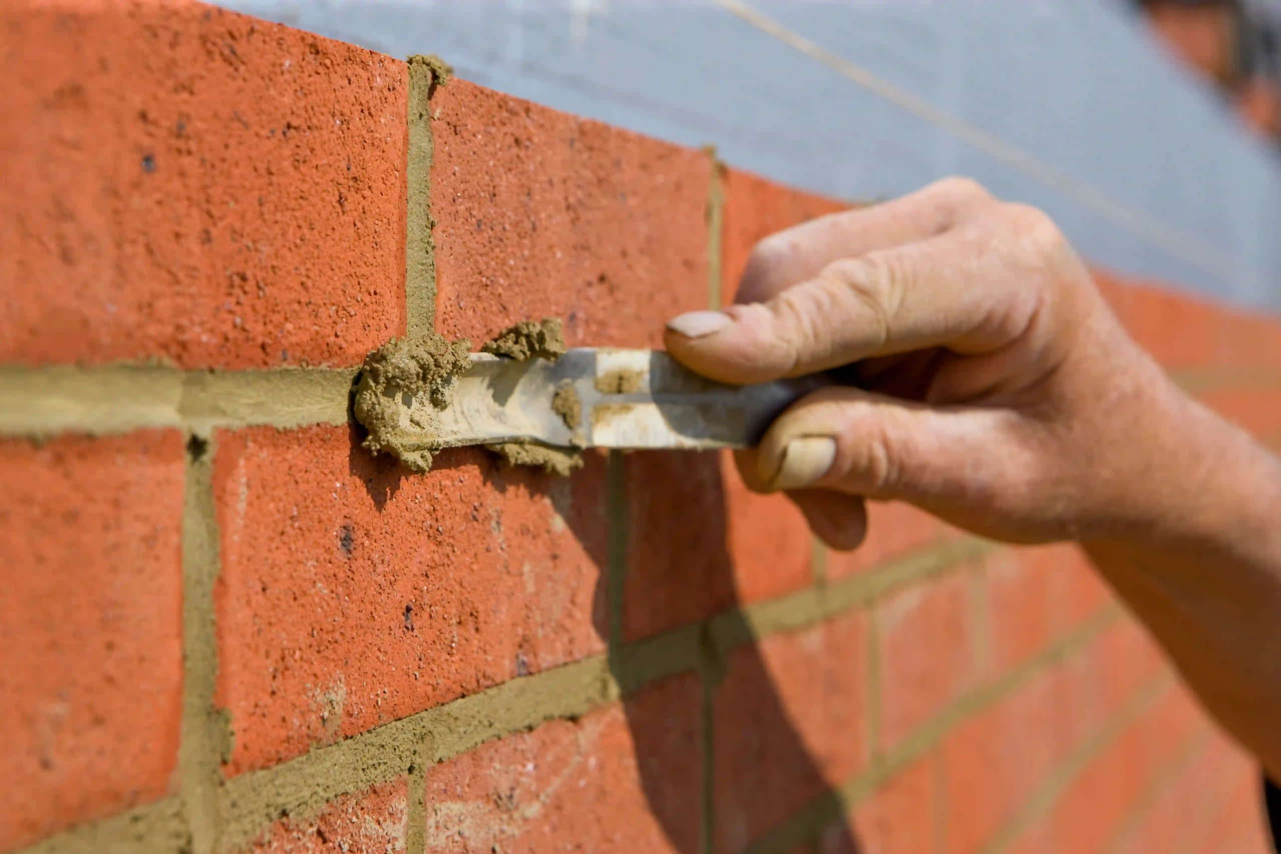 Mason using a jointer to smooth mortar between bricks.