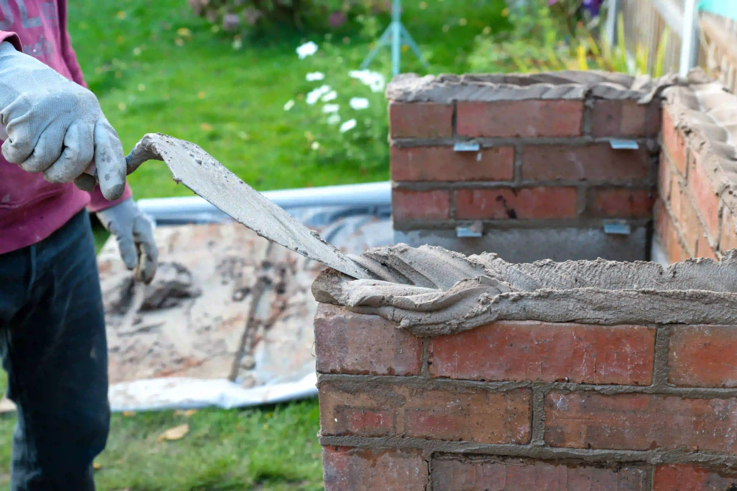 Mason applying mortar to a brick wall with a trowel.