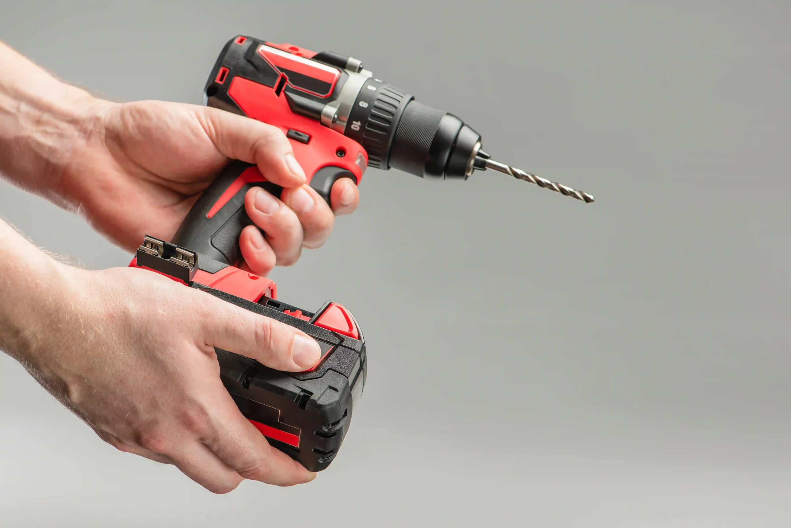 Hands holding a cordless drill with battery pack and drill bit