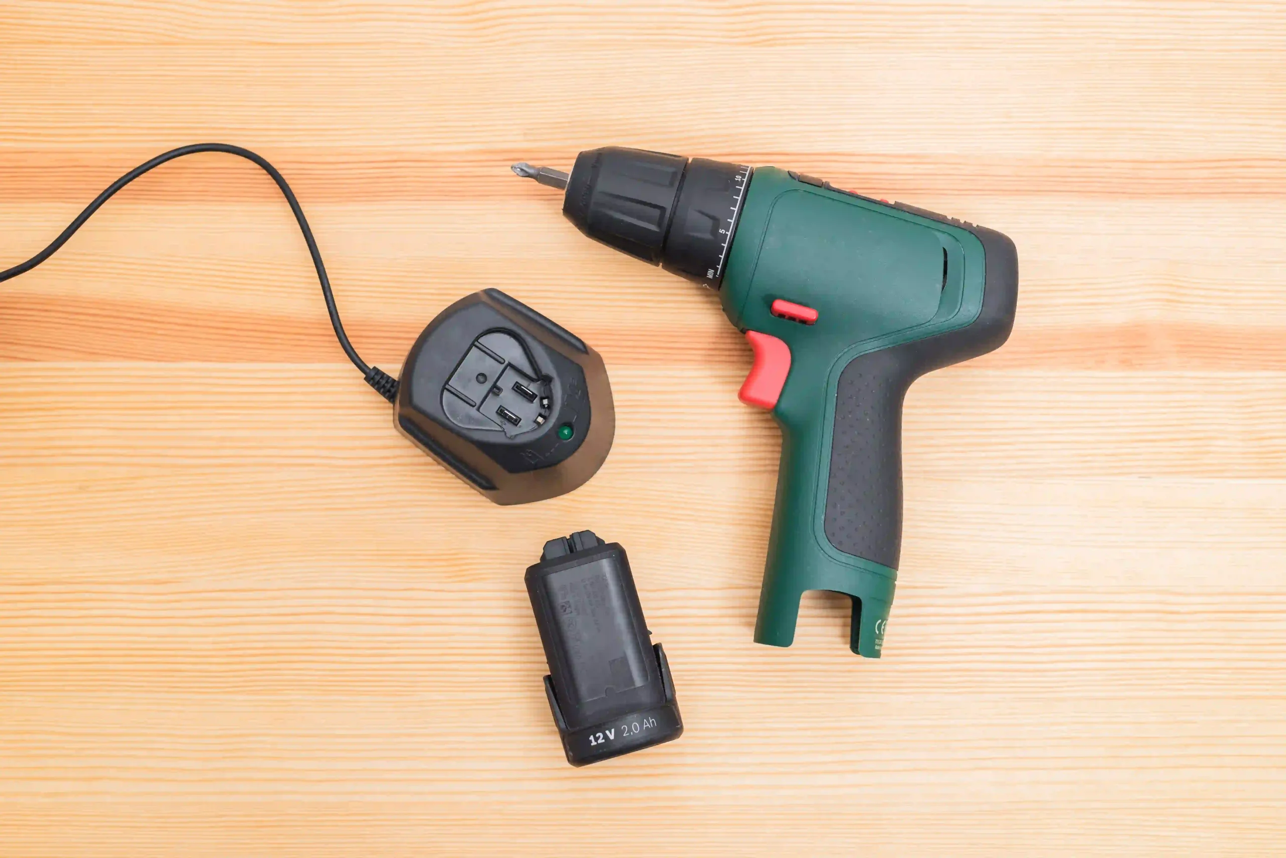 Taladro inalámbrico con batería y cargador de 12V sobre una mesa de madera.