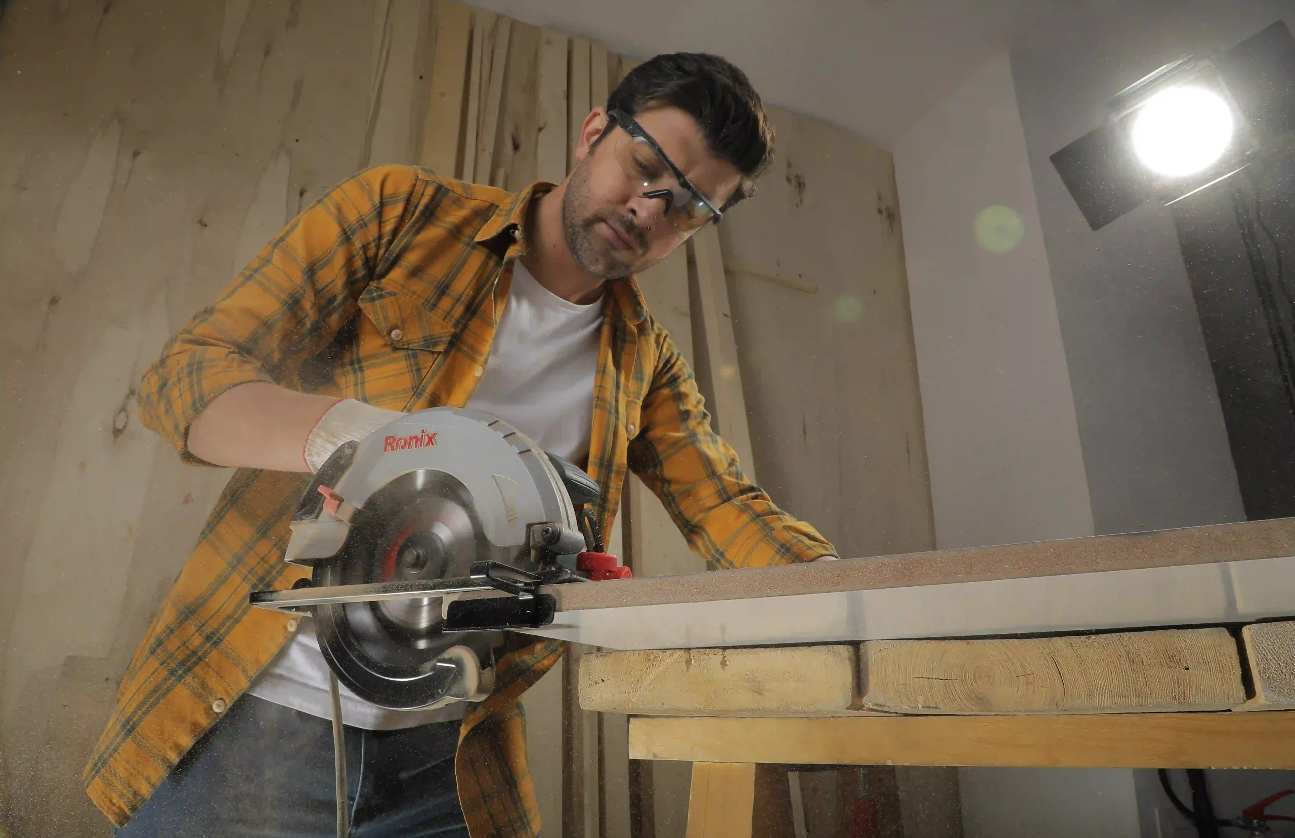Carpintero realizando un corte longitudinal con una sierra circular sobre un tablero de madera